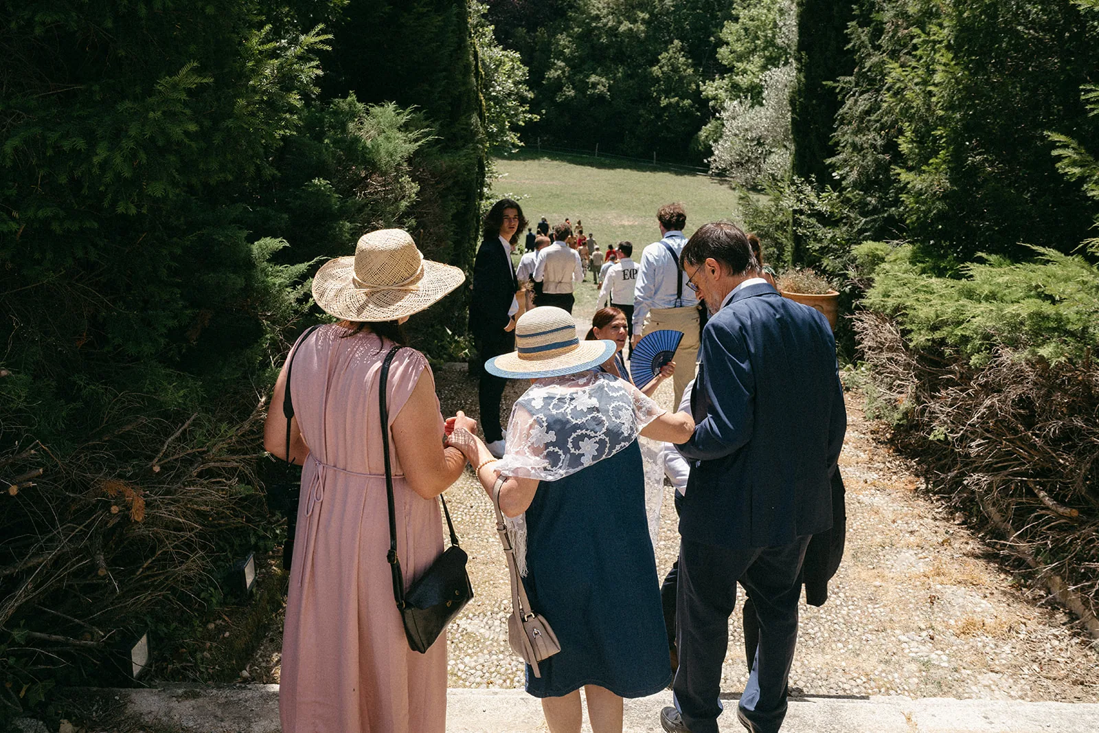 Des invités descendent l'allée du jardin pour rejoindre une cérémonie de mariage au Domaine de Camboyer
